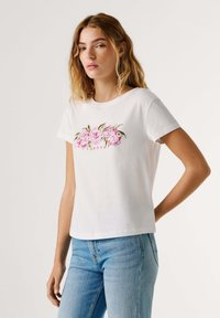 Λευκό βαμβακερό T-shirt με στρογγυλή λαιμόκοψη, κοντά μανίκια και ροζ κεντήματα με λουλούδια που περιλαμβάνουν τη λέξη «Λονδίνο». Συνοδεύεται από ανοιχτόχρωμο τζιν παντελόνι.