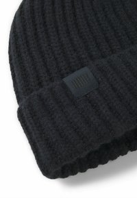 Gebreide zwarte beanie van zachte wol met een geribbeld patroon, met een klein zwart label met verticale lijnen op de omgevouwen rand.