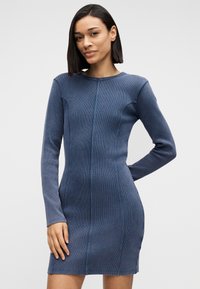 Το φόρεμα από τζιν έχει μακριά μανίκια, στρογγυλή λαιμόκοψη και εφαρμοστή γραμμή. Το χρώμα είναι σκούρο μπλε με ανάγλυφο, ριγωτό σχέδιο.