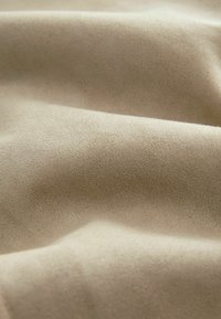 Soft beige fabric with a smooth texture, showcasing gentle drapes and creases. The material appears lightweight and fine in quality.