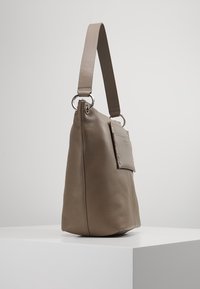 Beige läderhandväska med en slät textur, stor kropp och en sidoficka. Har en bred axelrem och metallackcenter.