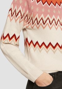Strickpullover mit einer cremefarbenen Basis, die ein Zickzackmuster in verschiedenen Schattierungen von Pink, Orange und Rot aufweist. Mit gerippten Bündchen und einem runden Halsausschnitt.