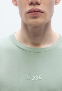 Light green crewneck t-shirt made of soft fabric, featuring a subtle embossed "BOSS" text in a lighter shade on the front.