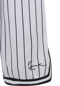 Biały materiał z pionowymi czarnymi cienkimi paskami oraz czarnym haftowanym podpisem w pobliżu dolnej krawędzi z czarną lamówką.