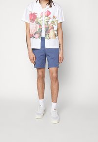 Kortärmad vit skjorta med en färgglad blommig tryck, tillsammans med blå shorts och vita sneakers. Har en avslappnad passform och knappstängning.