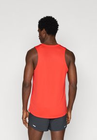 Piros sportos ujjatlan póló, letisztult dizájnnal, ujjatlan szabással és sima textúrával. Fekete rövidnadrággal viselve, fehér akcentusokkal.