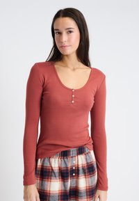 Top de color óxido de manga larga y cuello redondo con textura acanalada y detalle de tres botones en el escote, combinado con pantalones cortos de dormir de cuadros.