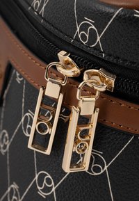 Zwarte gestructureerde tas met gouden hardware ritsen, bruine leren accenten en witte geometrische patronen op het oppervlak.