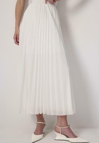 White pleated skirt with a high waist and elastic band. Lightweight fabric with a smooth texture, paired with white ankle-strap heels.
