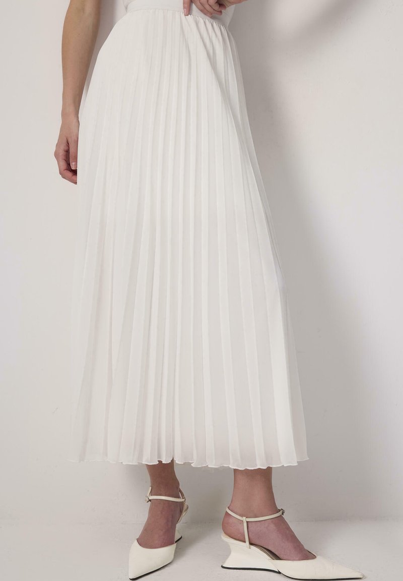 White pleated skirt with a high waist and elastic band. Lightweight fabric with a smooth texture, paired with white ankle-strap heels.