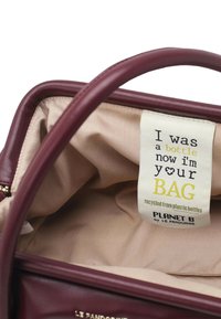 Borsa color bordeaux con esterno liscio, fodera interna beige e un'etichetta con la scritta "Ero una bottiglia, ora sono la tua BORSA, riciclata da bottiglie di plastica."