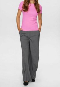 Różowa koszulka z krótkim rękawem w zestawie z szerokimi spodniami w szaro-płaszczowej kratkę. Spodnie mają boczne kieszenie i luźny krój. Czarne buty dopełniają całość.