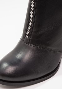 Černá kožená kotníková bota s hladkým povrchem, kulatou špičkou a stříbrným zipem na boku. Minimalistický design s nízkým, plochým podpatkem.