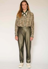 Blouse à motifs verts associée à un pantalon en simili cuir olive et des baskets blanches. Comprend une coupe ample et un design à boutons.