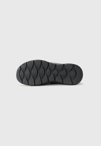 Semelle de chaussure en caoutchouc noir avec une surface texturée et à motifs. Présente des rainures ovales pour une meilleure accroche et une transition fluide vers la zone du talon.