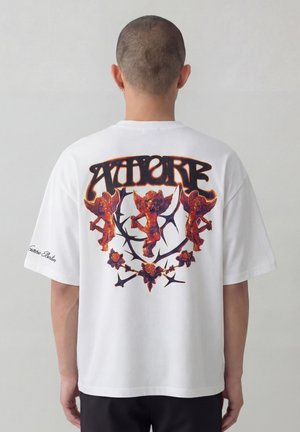 Persoon met kort haar draagt een wit T-shirt met drie oranje cherubs, een doornige wijnstok en gestileerde tekst op de achterkant.