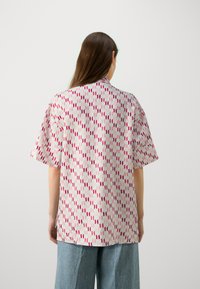 Cămașă cu mânecă scurtă dintr-un material ușor, având un model geometric în nuanțe de roz și roșu pe un fundal deschis. Croită lejer, cu guler rotund.