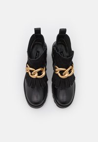 Černé kotníkové boty s lesklou koženou špičkou, svrškem ze semiše, třásněmi a zlatým řetízkem na přední straně.