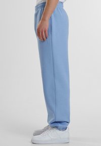 Helle blaue Sweatpants mit einem elastischen Bund und seitlichen Taschen, die ein tailliertes Design und gerippte Akzente an den Bündchen aufweisen. Kombiniert mit weißen Sneakers.