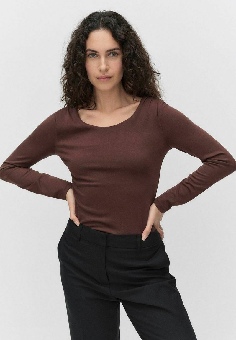 Långärmad brun topp i mjukt tyg med en rundad halsringning. Matchad med svarta byxor som framhäver en figurnära silhuett.