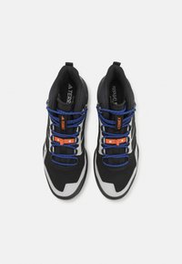 Des chaussures de sport noires avec une tige en maille, des lacets bleus et des accents orange. Conçues avec une semelle texturée et un col rembourré.
