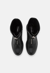 Botas de tobillo de cuero negro con cremallera lateral, punta redondeada, textura suave y diseño minimalista. El forro interior muestra el logo de la marca.