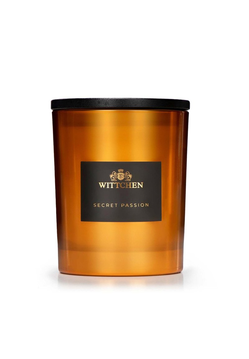 Barattolo di candela in vetro ambra con coperchio nero e un'etichetta con testo oro: "WITTCHEN SECRET PASSION." Texture liscia, forma cilindrica.