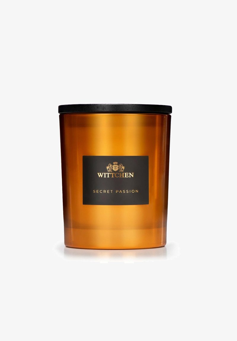 Barattolo di candela in vetro ambra con coperchio nero e un'etichetta con testo oro: "WITTCHEN SECRET PASSION." Texture liscia, forma cilindrica.