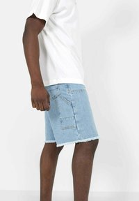 Shorts in denim azzurro chiaro con orlo sfrangiato, dotati di tasche laterali e una vestibilità rilassata, abbinati a una T-shirt bianca casual.