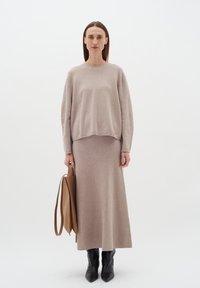 Ilgas šviesiai rudas megztinis ir deranti sijonas, suporuoti su juodais aštriais kulkšnių botais ir tan spalvos rankine. Lygus paviršius, paprastas dizainas.