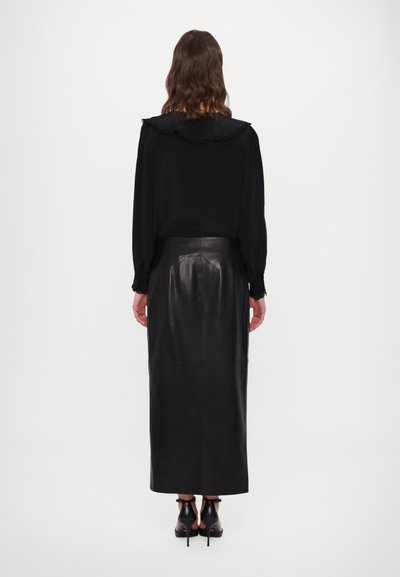 Camisa negra de manga larga con cuello rizado, combinada con una falda midi de cuero negro, que muestra una textura suave y una silueta ajustada.