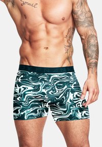 Boxerbriefs med ett svängt mönster i grönt och vitt. Tillverkade av elastiskt tyg, med ett enfärgat svart midjeband som visar varumärkesnamnet.