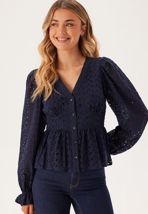 Blusa blu navy con dettagli in occhiello, scollatura a V, apertura con bottoni e maniche a sbuffo, caratterizzata da un corpino aderente e orlo peplum.