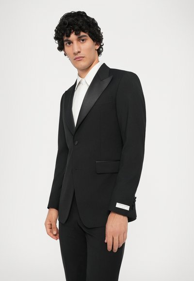 Čierna smokingová sako so saténovými klopami, zapínanie na jeden gombík a predné vrecká. Spárované s bielou košeľou. Štíhly strih.