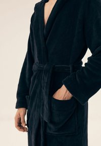 Granatowy szlafrok wykonany z miękkiego, pluszowego materiału z kołnierzem szalowym, z paskiem w talii i dwiema przednimi kieszeniami. Charakteryzuje się luźnym krojem.