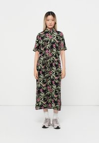 Robe noire à motifs floraux avec des orchidees roses et des feuilles vertes, dotée d'une taille ceinturée et de manches courtes, associée à des baskets légères roses.