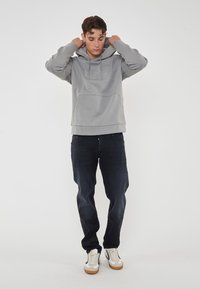 Felpa grigia con tasca a marsupio e dettagli del logo, abbinata a jeans scuri e sneakers. Tessuto morbido e vestibilità rilassata.