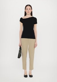 Top ajustat, negru, cu umărul gol, asociat cu pantaloni crema, cu croială conică și sandalii negre. Modelul ține o geantă verde cu embossing croco. Design simplu și elegant.