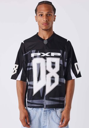 Jeune homme aux cheveux tressés portant un maillot de sport noir et gris avec les logos "PXP" et un grand "08", associé à un jean bleu clair.