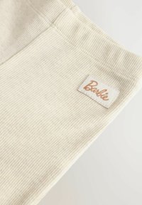 Gros plan sur un tissu côtelé crème avec une étiquette rectangulaire cousue indiquant Barbie en écriture cursive marron.
