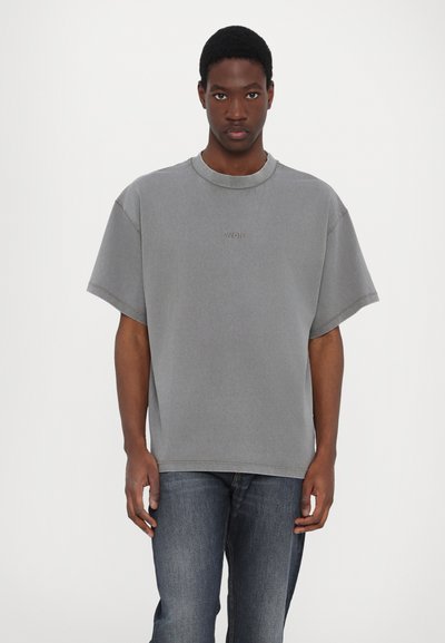 Grå oversized t-shirt med korta ärmar, med en ribbad rundhals och diskret "WON"-logotyp på bröstet, tillverkad av mjukt bomullstyg.