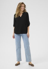Blusa nera con scollatura a V e maniche a giro, abbinata a jeans a gamba dritta blu chiaro e scarpe basse marroni.