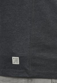 Mørkegrå T-shirt lavet af blødt stof, med et lille mærke i bunden, der indeholder brandinformation og produktdetaljer.
