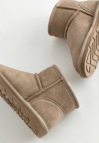Bottines en suede tan avec une texture douce, présentant des détails cousus et une semelle en caoutchouc avec un motif de bande de roulement.