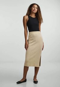 Beige knit midi skirt with side slit, paired with a fitted black sleeveless top and black flats. Smooth texture, simple design, straight silhouette.