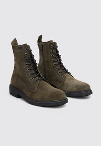 Botas de ante verde oscuro hasta el tobillo con punta redonda, cordones en la parte delantera, cremallera lateral y suela de goma negra. Cuenta con detalles de costura.