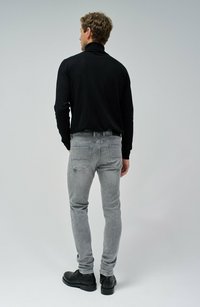 Camisa negra de manga larga, jeans grises ajustados y botas negras con cordones. Incluye un collar alto y un sutil pespunte en el bolsillo trasero.