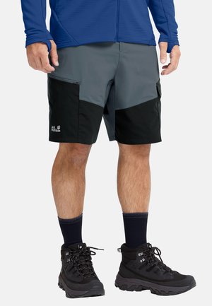 Uomo che indossa pantaloncini da outdoor grigi e neri, stivali da trekking neri, calzini scuri e una maglia a maniche lunghe blu con fori per i pollici.