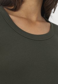 Mörkgrön strukturerad tyg med ett åtsittande ribbat mönster och rund halsringning. Inga synliga sömmar eller utsmyckningar.