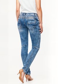 Jeans skinny blu con una texture sbiadita, dettagli di cucitura, due tasche posteriori e vita media. Indossati con tacchi alti marroni.